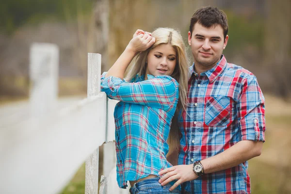 Portrait de jeune couple heureux portant des chemises s'amusant en plein air près de la clôture dans le parc — Photo