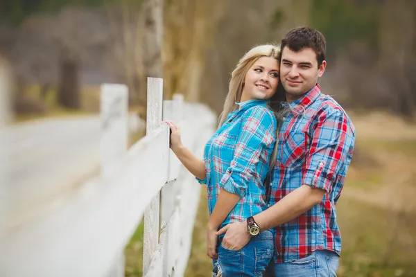 Portrait of happy young couple wearing shirts having fun outdoors near fence in park — Stock Photo, Image