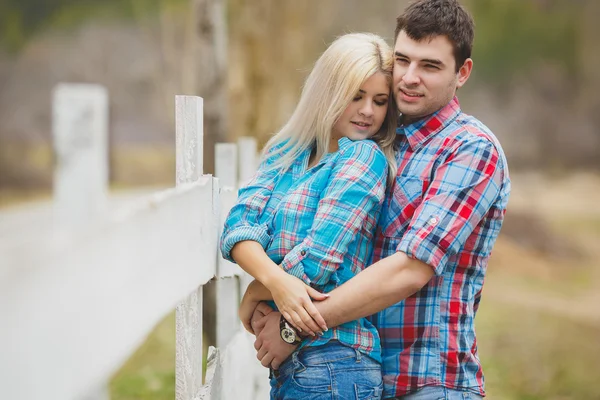 Portret van gelukkige jonge paar dragen van shirts met plezier buiten in de buurt van hek in park — Stockfoto