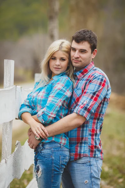 Retrato de jovem casal feliz vestindo camisas se divertindo ao ar livre perto de cerca no parque — Fotografia de Stock