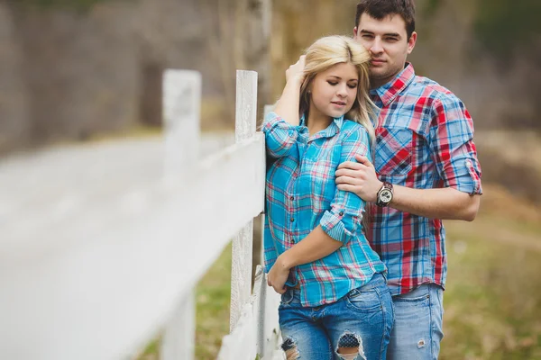 Retrato de jovem casal feliz vestindo camisas se divertindo ao ar livre perto de cerca no parque — Fotografia de Stock
