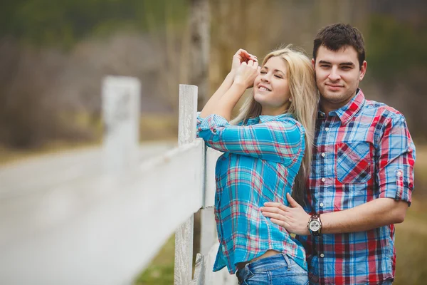 Portrait of happy young couple wearing shirts having fun outdoors near fence in park — Stock Photo, Image