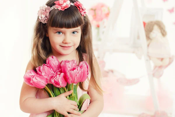 Nahaufnahme Porträt eines kleinen entzückenden Mädchens mit rosa Tulpen in den Händen. — Stockfoto