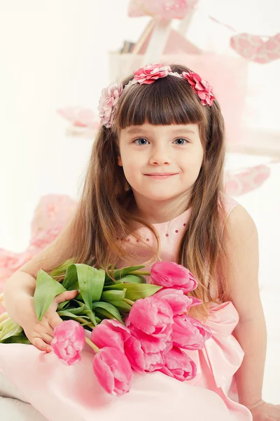Nahaufnahme Porträt eines kleinen entzückenden Mädchens mit rosa Tulpen in den Händen. — Stockfoto