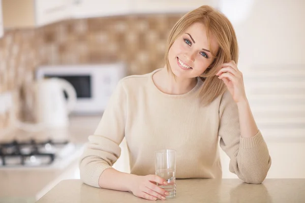 Mooie vrouw in de keuken met een glas water — Stockfoto