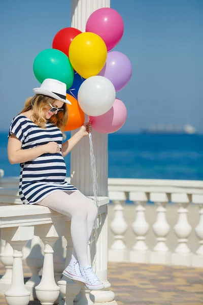 Mulher grávida em óculos de sol e um chapéu branco com balões — Fotografia de Stock