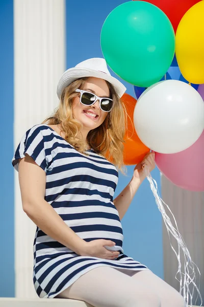 Hamile kadın güneş gözlüğü ve balonlar ile beyaz bir şapka — Stok fotoğraf