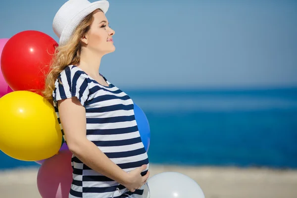 Gravid kvinna i solglasögon och en vit hatt med ballonger Royaltyfria Stockfoton