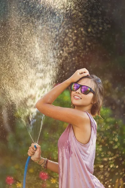 Beautiful woman watering roses with a garden hose — Stock Photo, Image