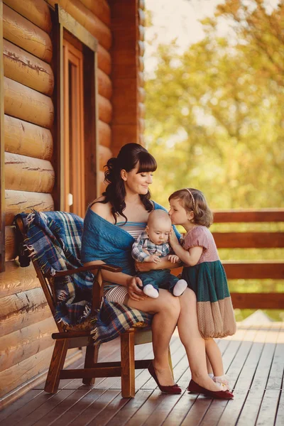 Мама с детьми, сидит рядом с деревянным домом — стоковое фото