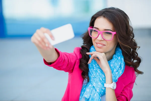 Happy young girl making funny face while taking pictures of herself through cellphone, over white background — Stock Photo, Image