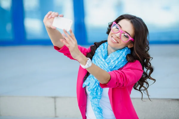 Happy young girl making funny face while taking pictures of herself through cellphone, over white background — Stock Photo, Image