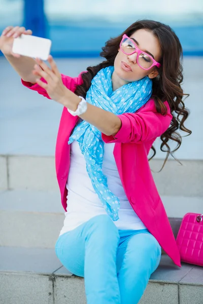 Chica joven feliz haciendo cara divertida mientras toma fotos de sí misma a través del teléfono celular, sobre fondo blanco — Foto de Stock