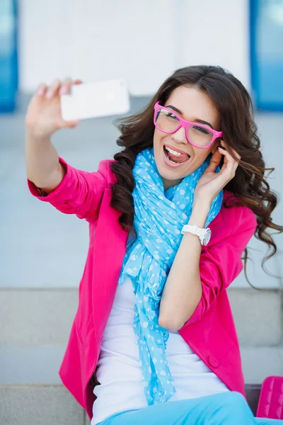 Chica joven feliz haciendo cara divertida mientras toma fotos de sí misma a través del teléfono celular, sobre fondo blanco — Foto de Stock