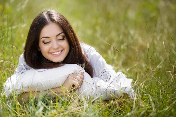 Het meisje met een kussen op het gras verse lente. — Stockfoto