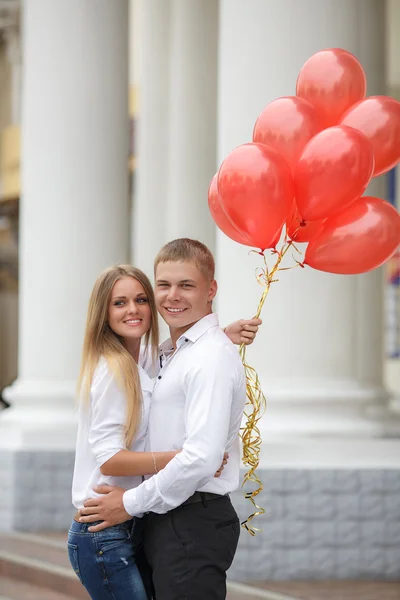 Mladý pár v lásce s červenými balóny na ulici — Stock fotografie
