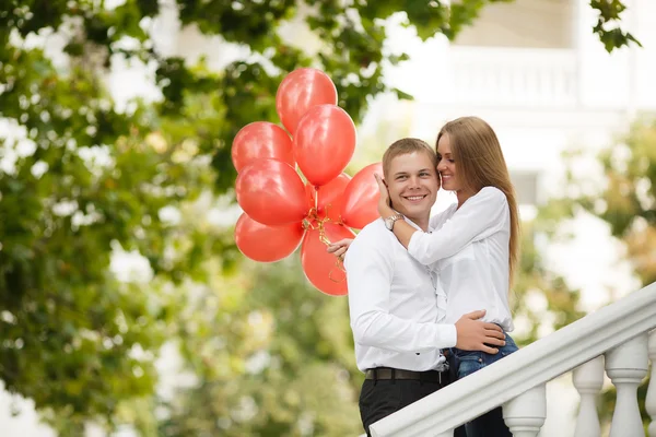 Ein junges verliebtes Paar mit roten Luftballons auf der Straße — Stockfoto