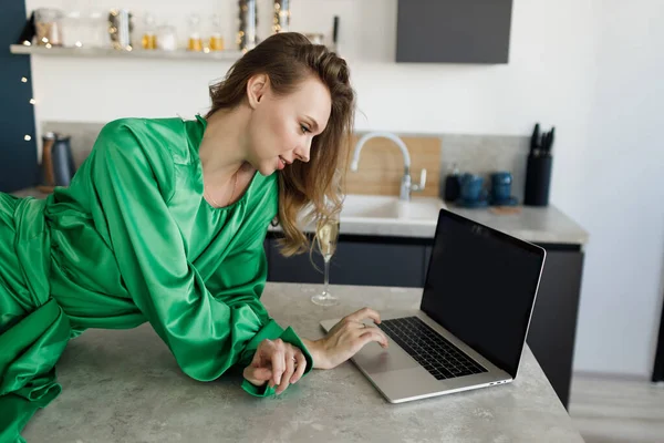 Joven mujer sonriente en vestido de moda en casa con ordenador portátil y champán — Foto de Stock