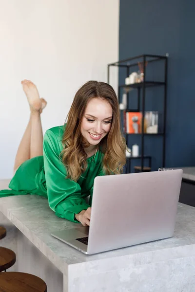 Giovane donna sorridente in abito a casa con computer portatile e champagne, lavoratore freelance — Foto Stock
