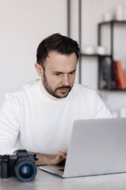 Evde çalışan dizüstü bilgisayarı ve kamerası olan yakışıklı fotoğrafçı.