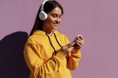 Kulaklıklı, genç, gülümseyen bir kadın telefonda konuşuyor.