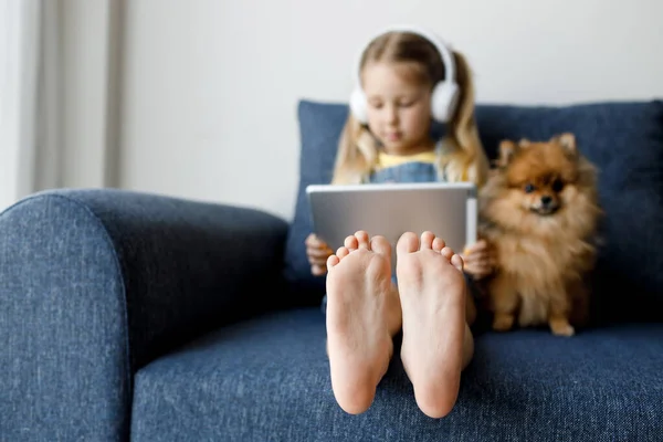 Roztomilá holčička doma se sluchátky a pomocí tabletu — Stock fotografie