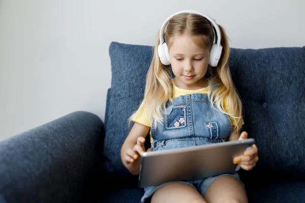 Roztomilá holčička doma se sluchátky a pomocí tabletu — Stock fotografie