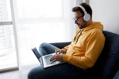 Evde çalışan dizüstü bilgisayarı ve kulaklığı olan yakışıklı adam.