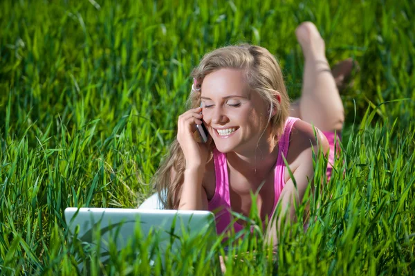 Ung kvinna med bärbar dator sitter på grönt gräs — Stockfoto