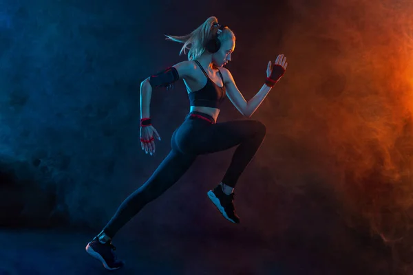 Sprinter uruchomić. Silna atletyczna kobieta biegająca na czarnym tle ubrana w strój sportowy. Motywacja fitness i sportu. Koncepcja biegacza. — Zdjęcie stockowe