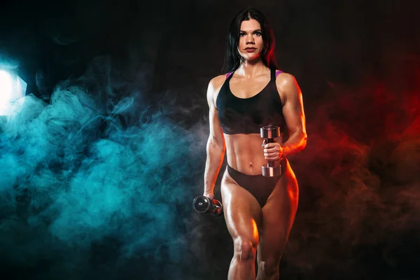 Sportlich fitte Frau, Athletin mit Kurzhanteln macht Fitnessübungen auf schwarzem Hintergrund. — Stockfoto