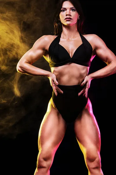 Silná sportovní žena v bikinách ukazuje svaly na černém pozadí. Sportovní koncepce — Stock fotografie