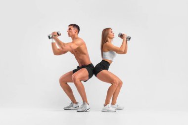 Spor salonundaki zinde çift, beyaz arka planda dambıllarla izole edilmiş. Fitness konsepti. Sağlıklı yaşam tarzı.