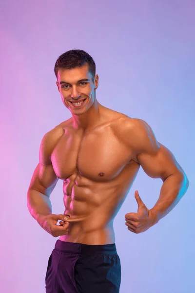Mutlu sporcu adam vücudunda ne kadar az deri altı yağ olduğunu gösteriyor. Sporcular renkli arka planda izole edilmiş. Fitness motivasyonu. — Stok fotoğraf