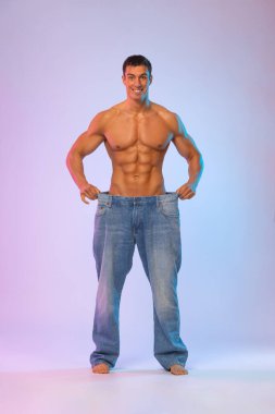 Genç adam büyük kotlarla ne kadar kilo verdiğini gösteriyor. Konsepte uygun yağ. Fitness posteri