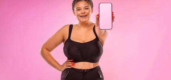 Dietetyczny szablon programu fitness. Dziewczyna demonstruje ekran smartfona do prezentacji aplikacji mobilnej. Gruba kobieta uśmiechnięta na różowym tle z telefonem w ręku. — Zdjęcie stockowe