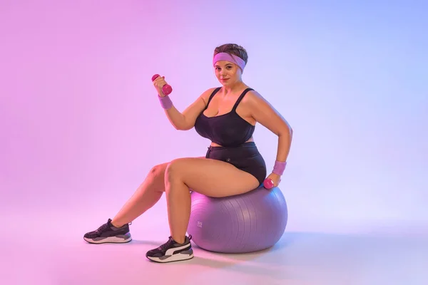 Größe plus Fitness-Modell, Athletiktrainer Trainerin Frau in der Heimfitness sitzen auf fitball isoliert auf rosa Hintergrund. Workout-Sportkonzept — Stockfoto