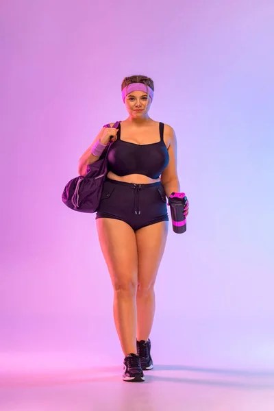 Ve al gimnasio. Talla más modelo mujer con bolso en ropa deportiva sobre fondo rosa. Deportes y estilo de vida saludable —  Fotos de Stock