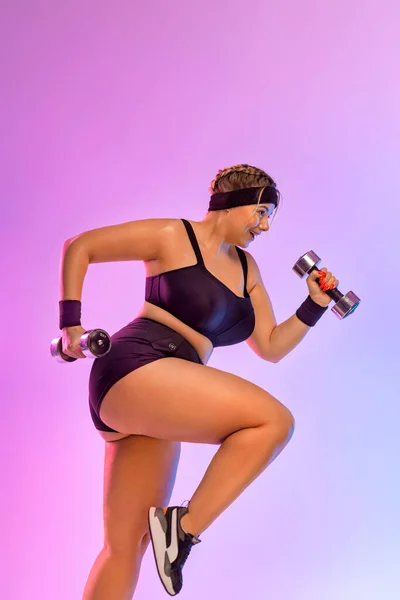 身体阳性的概念。尺寸加上带着哑铃跳的模特胖女孩想在粉红的背景下减肥. — 图库照片