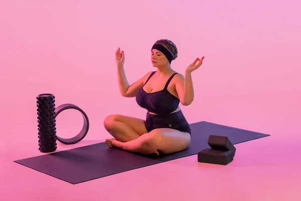Yoga. Retrato de gordura jovem praticando fitness indoor. Tamanho bonito mais modelo prática asana na classe. Calma e relaxe no fundo rosa. — Fotografia de Stock