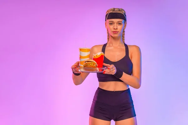 在粉色背景下摆出运动女运动员的姿势，并配上快餐菜单。关于健康或营养主题的社交媒体出版物的想法. — 图库照片