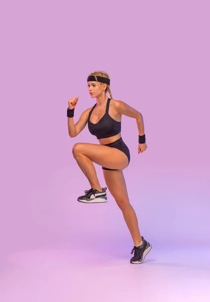 Sprinter se ejecuta en pleno crecimiento. Mujer atlética fuerte corriendo sobre fondo púrpura usando la ropa deportiva. Fitness y motivación deportiva. Concepto de corredor. —  Fotos de Stock