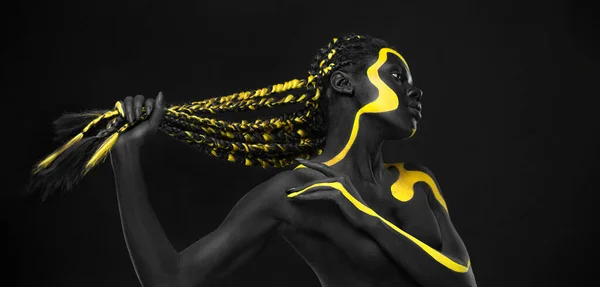 Yellow and black body paint. Woman with face art. Young girl with bodypaint. An amazing model with makeup.