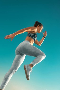 Koşucu konsepti. Koşu. Gökyüzünde koşan güçlü atletik kadın spor kıyafetlerini giyiyor. Spor ve spor motivasyonu.