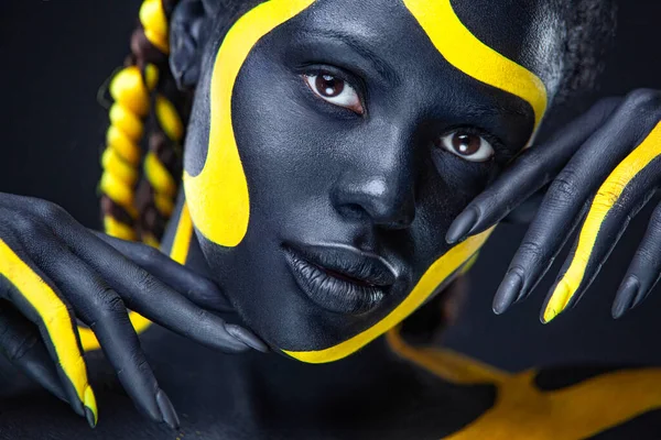 Yellow and black body paint. Woman with face art. Young girl with colorful  bodypaint. An amazing afro american model with makeup. Stock Photo