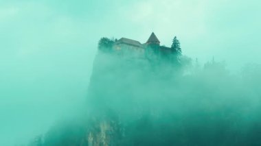Lake Bled castle in blue clouds. Dramatic view on Blejski grad. Foggy castle on mountain. Handheld shot. Lake Bled, Slovenia.