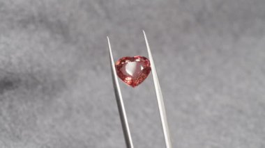 Kırmızı kalp şeklinde turmalin mücevher cımbızda. Doğum günü için mücevher alışverişi, Sevgililer Günü, diğer tatiller. Gemolojist ya da kuyumcu elinde kırmızı turmalin, gri arka planda makro çekim