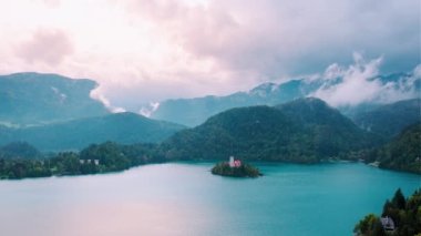 Lake Bled in Slovenia. Sunset view from above on Assumption of Maria Church against cloudy Julian Alpine mountains. Church reflecting in lake Bled waters. Handheld panning shot.