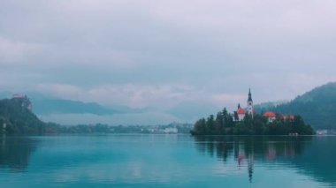 Slovenya 'da Kan Gölü. Bulutlu Julian Alpine dağlarına karşı Maria Church 'ün Varsayımı üzerine gün batımı görüşü. Kan gölündeki suları yansıtan bir kilise. El kamerasıyla..