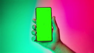 Mobile phone in hand. Holding smartphone with changing colorful red blue green background. Green chromakey screen with markers. Hand lifts phone up and holds it still.